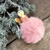 Pink pompom angel tree decoration with wooden face and wings hanging by a pine branch