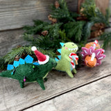 Three felt standing Christmas dinosaurs on a wooden table