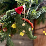 Green felt dinosaur with red spikes and Santa hat hanging on a tree