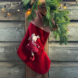 Red knitted Christmas stocking with a decorative mouse, hanging by a festive garland