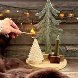 White Christmas tree candle being lit beside a felt tree and taper candle