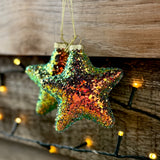 Multi-coloured sparkly star tree decoration hanging in front of fairy lights