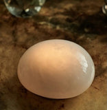Soft White LED rechargeable glass pebble light glowing on a wooden table