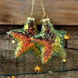 Two multi-coloured sparkly star tree decorations hanging from gold thread