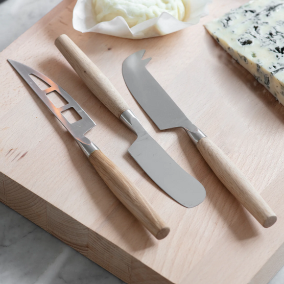 Three cheese knives on a wooden cutting board with a block of blue cheese.