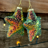 Pair of sparkly star tree decorations against a wooden wall with fairy lights