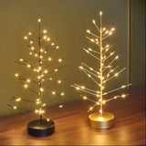 Black and gold Mini Festive LED trees lit up on a wooden table